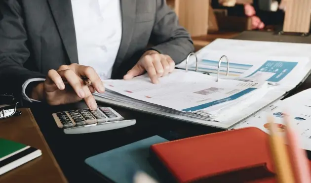 A person reviewing reports while using a calculator to analyse data.