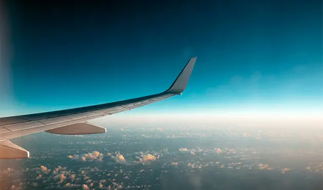 View from an airplane window showing an aircraft wing extending over clouds.